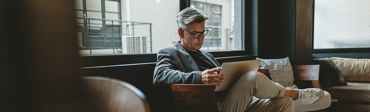 Homem de óculos sentado em uma poltrona moderna em um ambiente corporativo, usando um laptop.