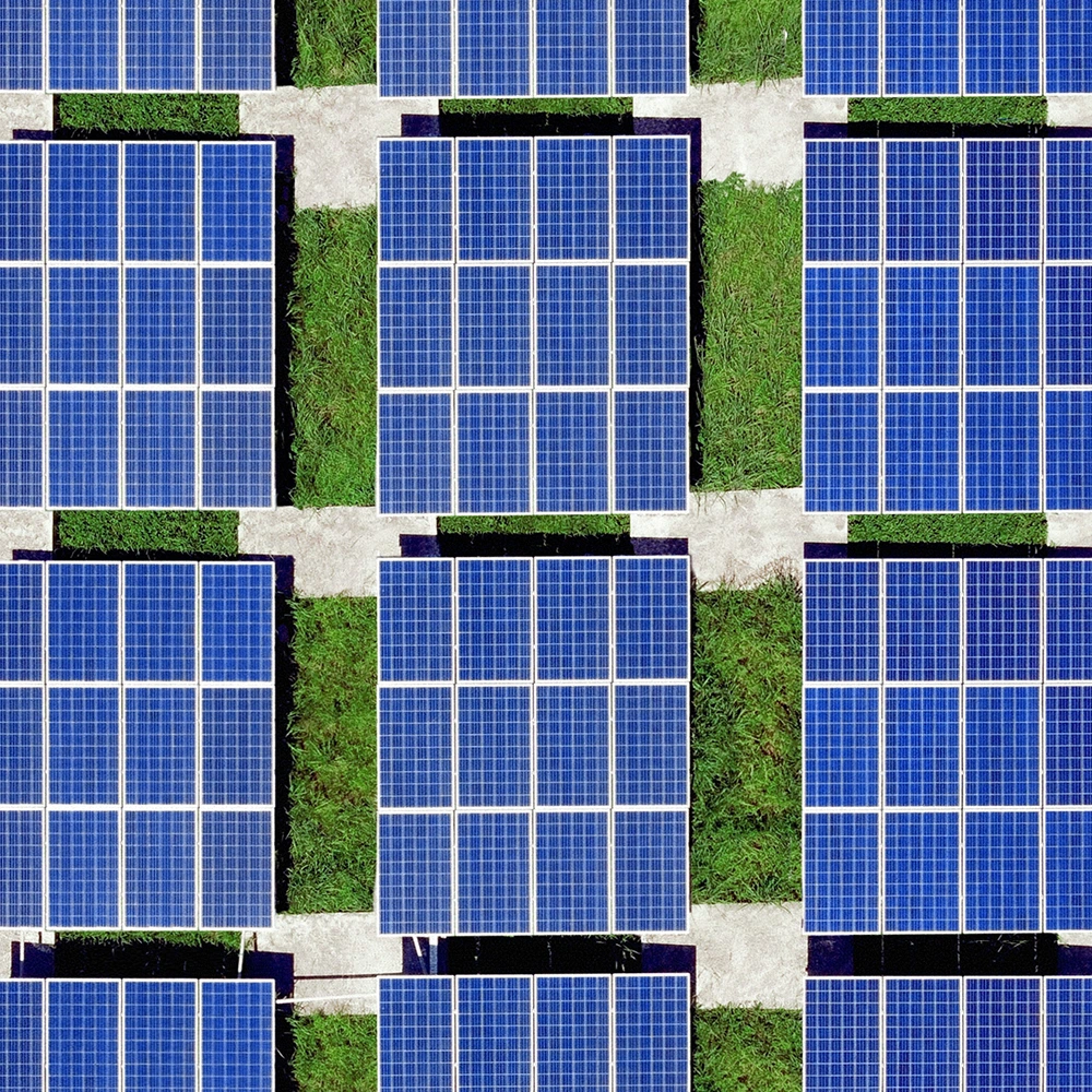 Vista aérea de uma usina solar com fileiras organizadas de painéis fotovoltaicos azuis instalados sobre áreas gramadas, intercaladas por caminhos de acesso.