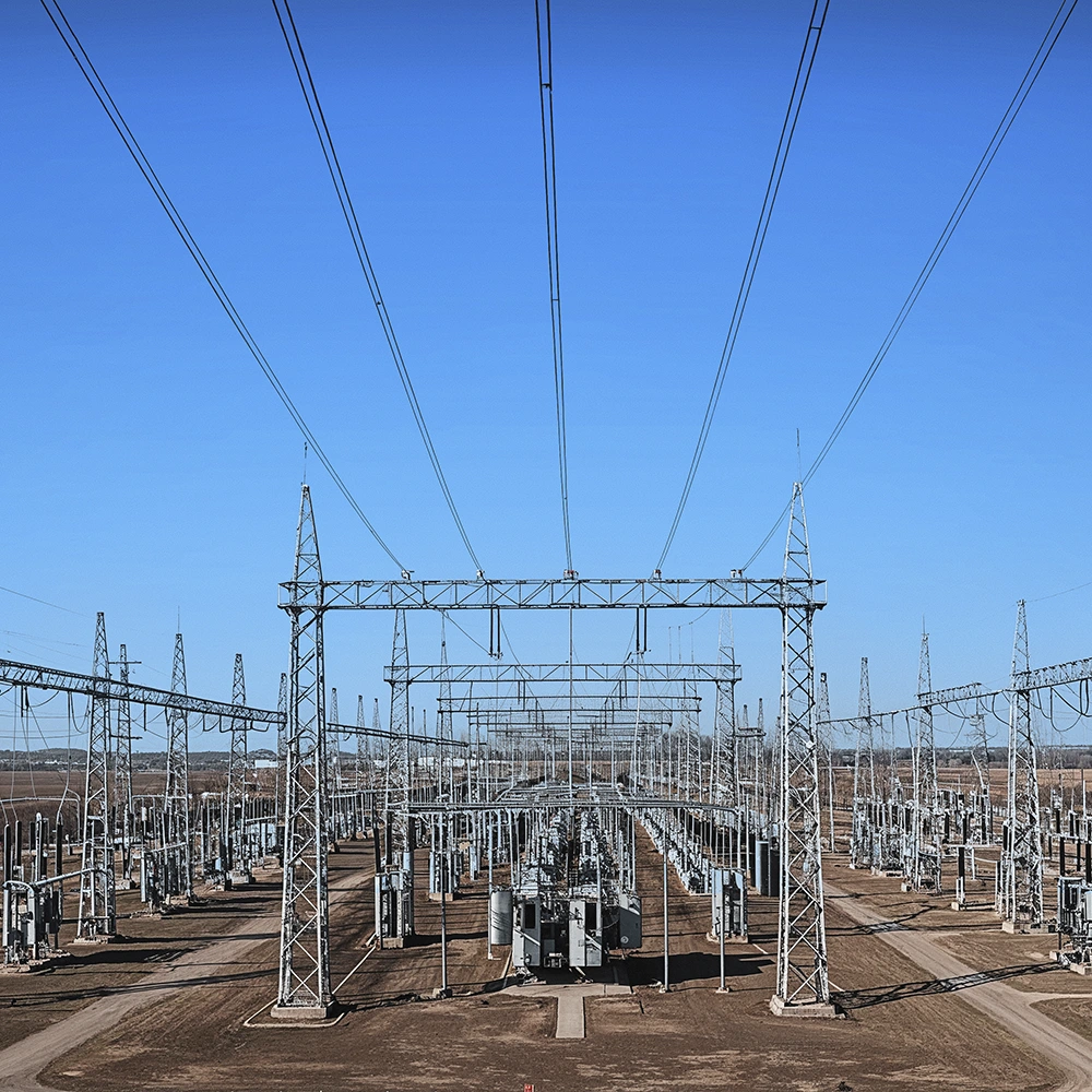 Subestação de energia elétrica ao ar livre, com estruturas metálicas, transformadores e linhas de transmissão interligadas, em área aberta sob céu azul.