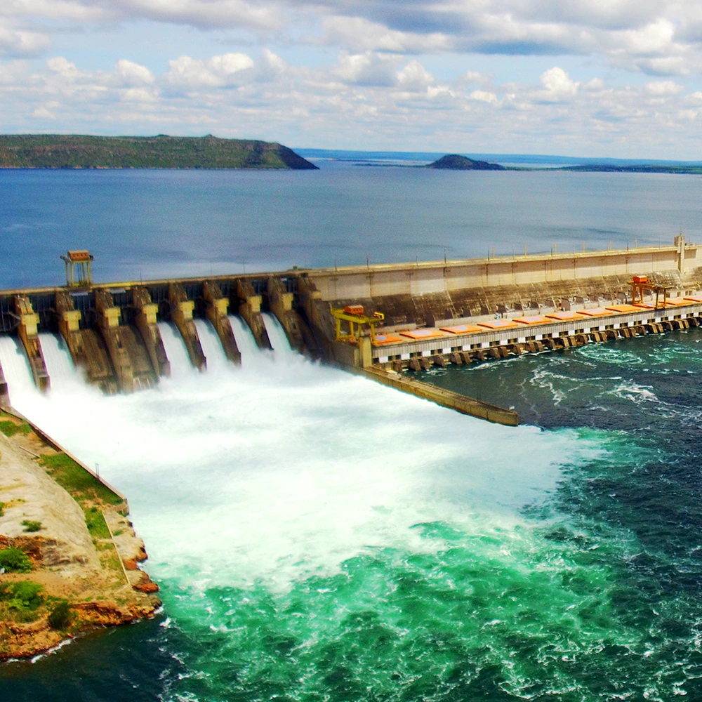 Vista aérea de uma usina hidrelétrica com vertedouro em operação, liberando grande volume de água para o rio abaixo da barragem.