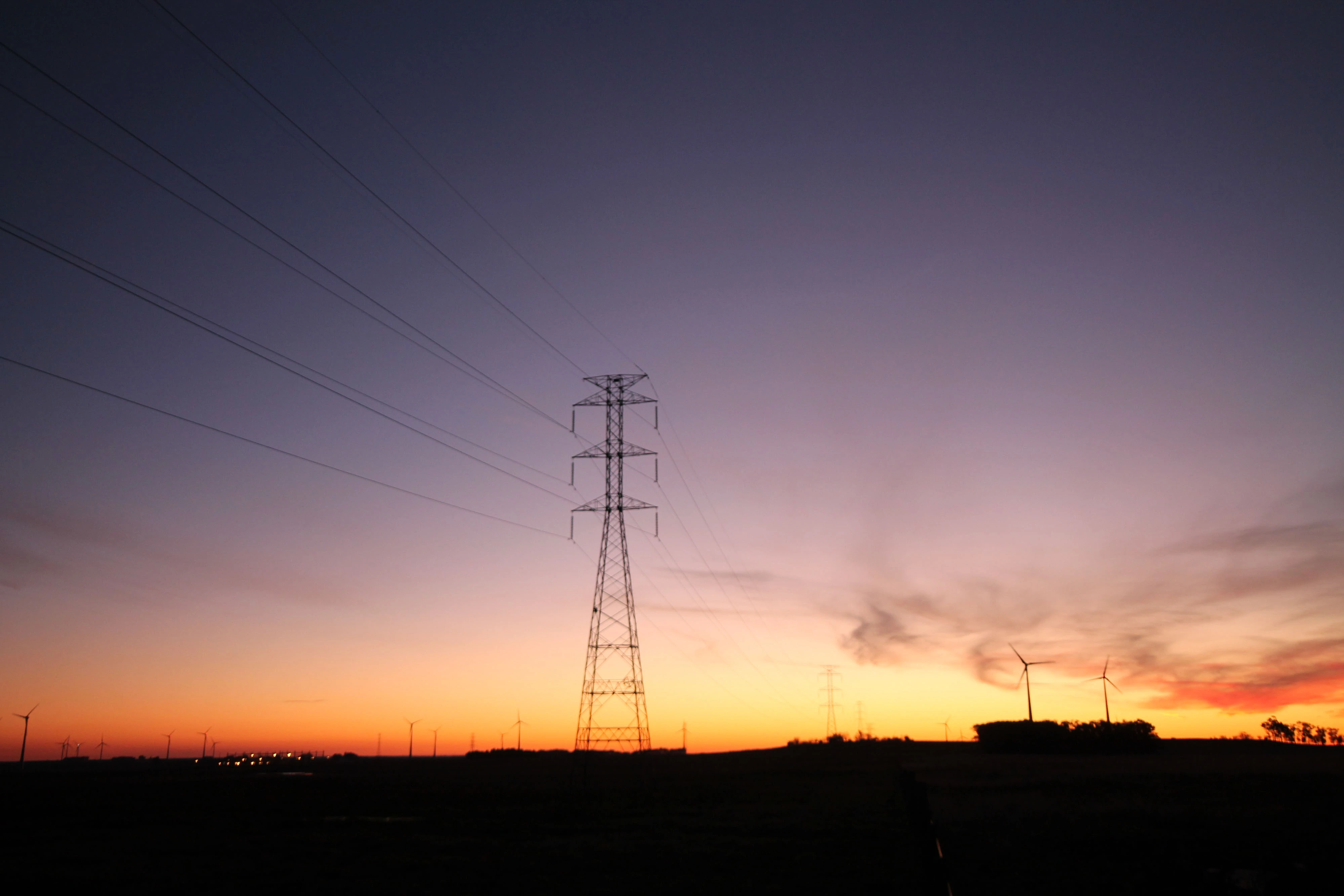 Por do sol com torre de transmissão e duas turbinas eólicas ao fundo