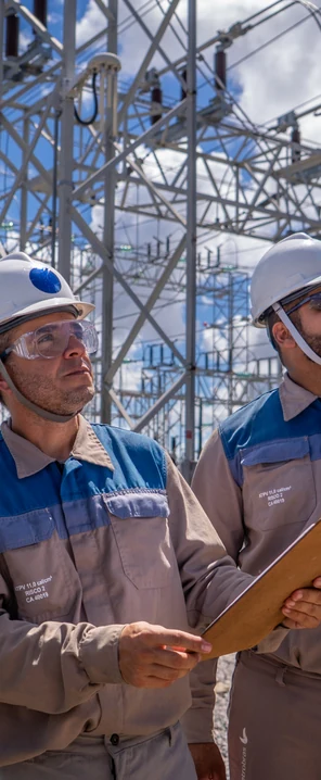 Profissionais da AXIA Energia em ambiente de trabalho, com estruturas de transmissão de energia ao fundo.