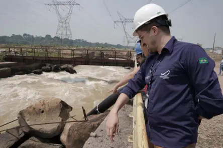 Profissionais em área operacional de usina hidrelétrica monitoram o fluxo de água próximo às estruturas da barragem.